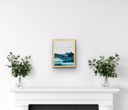 Painting of a blue mountain scene, hanging in a natural wood frame