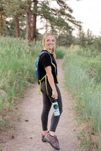 Load image into Gallery viewer, The artist Meg Elaine Miller hiking with a water bottle covered in her sticker pack. Mountain adventure themed stickers with mountains, pine trees, and &quot;climb on&quot; for rock climbing or hiking
